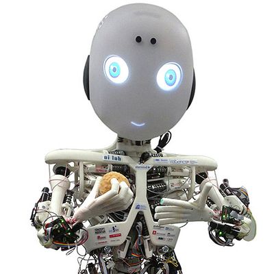 A child-like skeletal robot with musculature and electronics are exposed. Its head is egg shaped with glowing blue eyes and mouth. 