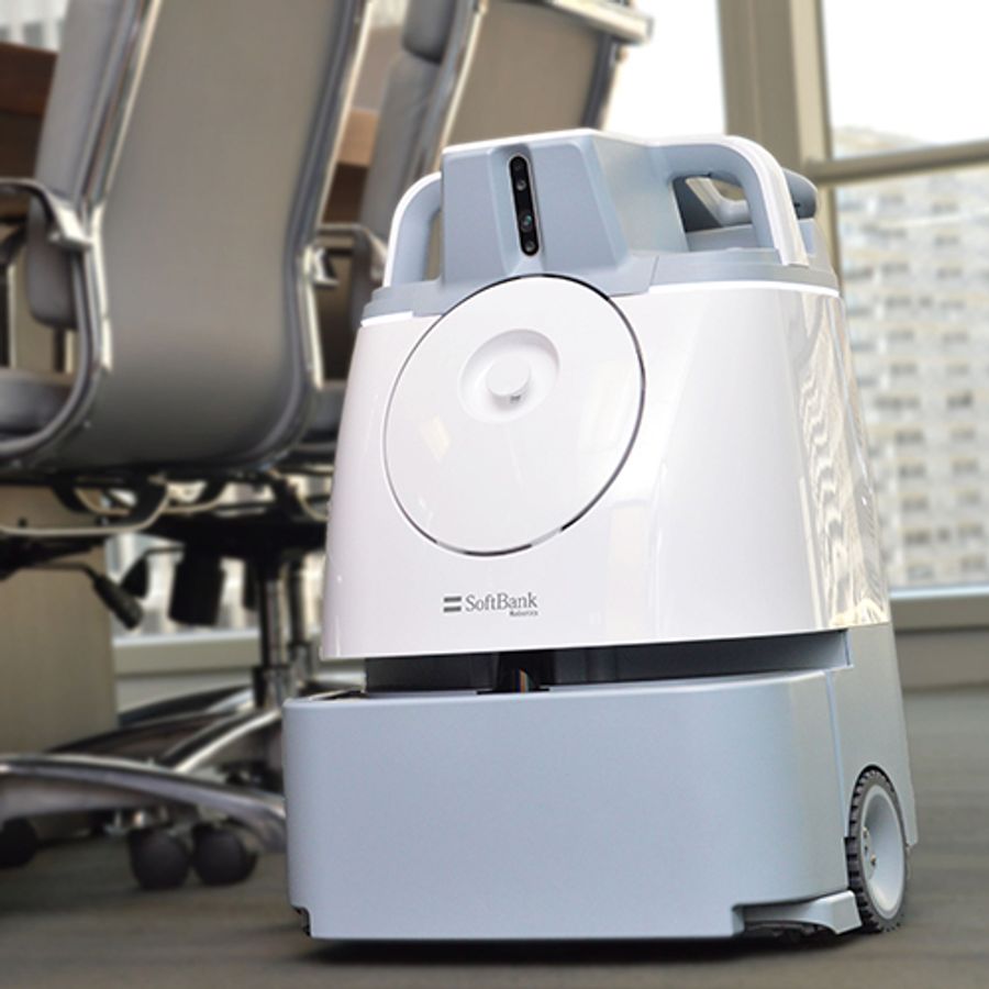 A white and gray boxy shaped robotic vacuum on a wheeled base rolls alongside office chairs in a conference room.