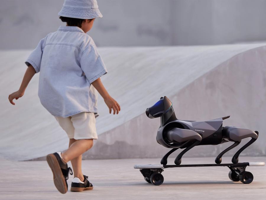 A young boy runs towards a small robotic dog on a skateboard.