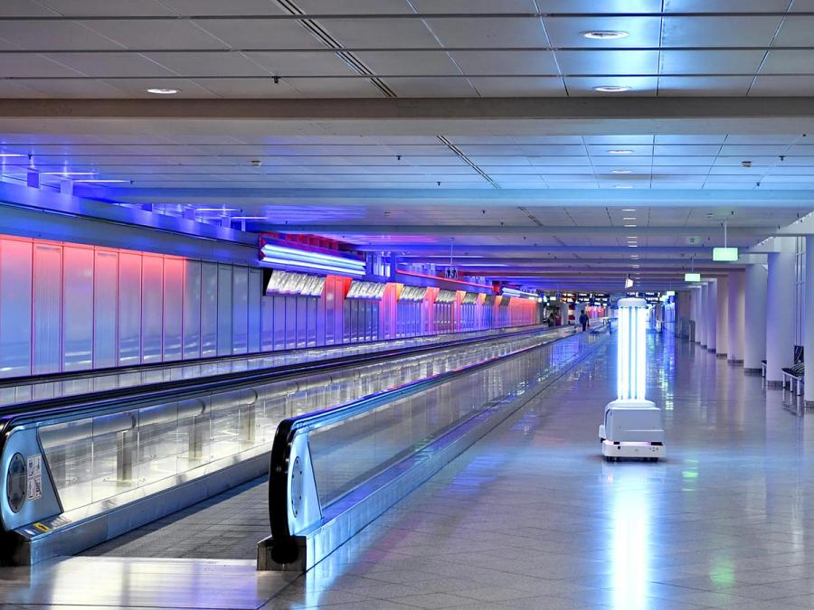 A mobile robot with bright UV lights moves through an empty airport next to a walkway. 