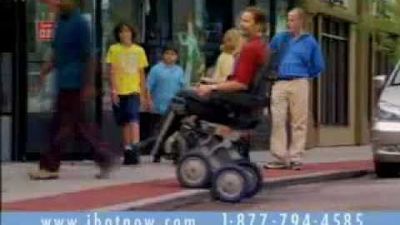 A man sitting on an iBOT powered wheelchair drives over a curb on a street. 