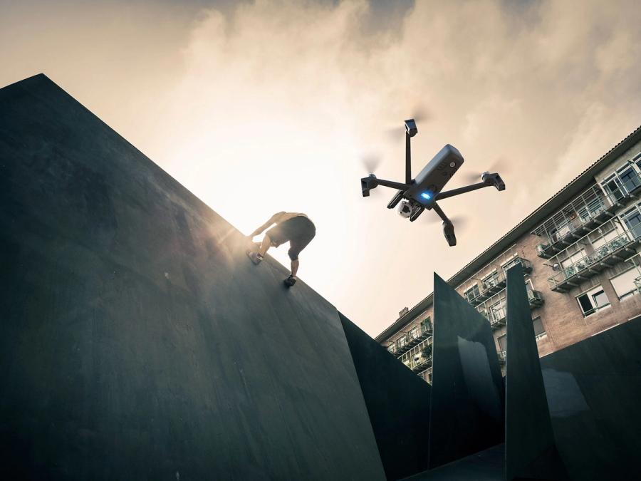 A drone hovers below a person climbing a wall.