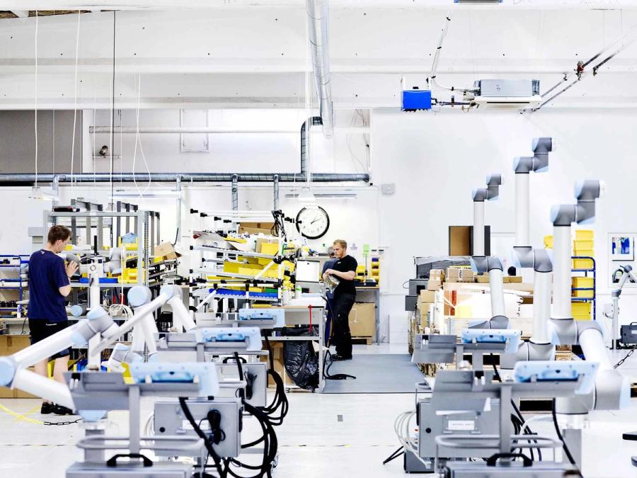 A wide photograph shows workers in a factory with many cobots.