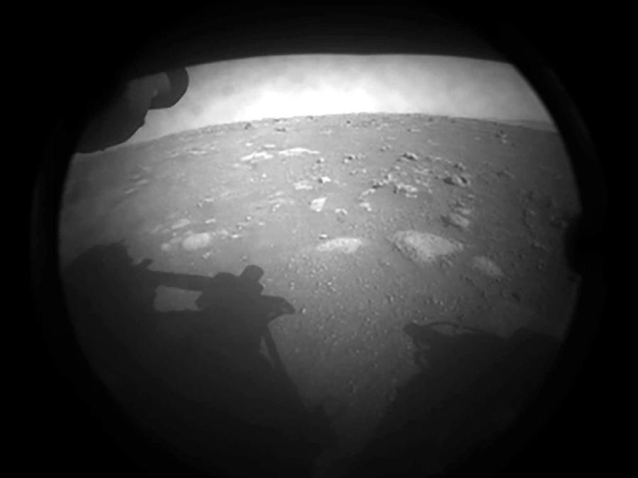 A black and white photo of a landscape with rocks and the shadow of the rover.