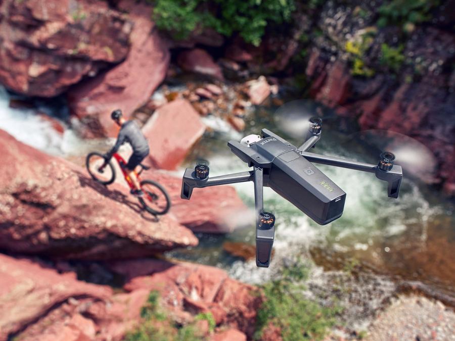 A drone flies over someone biking on rocky terrain.