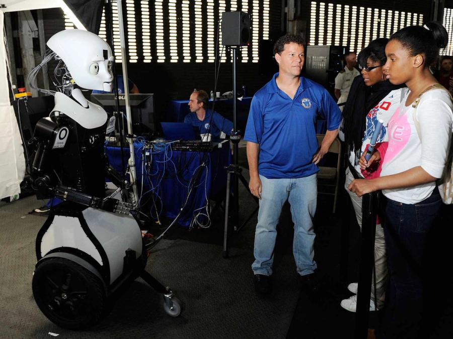 The human sized wheeled robot is facing many people in a lab.