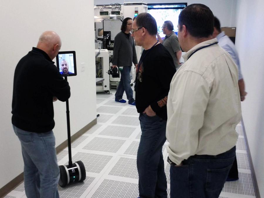 People in an office stand around a person seen on a telepresence robot.