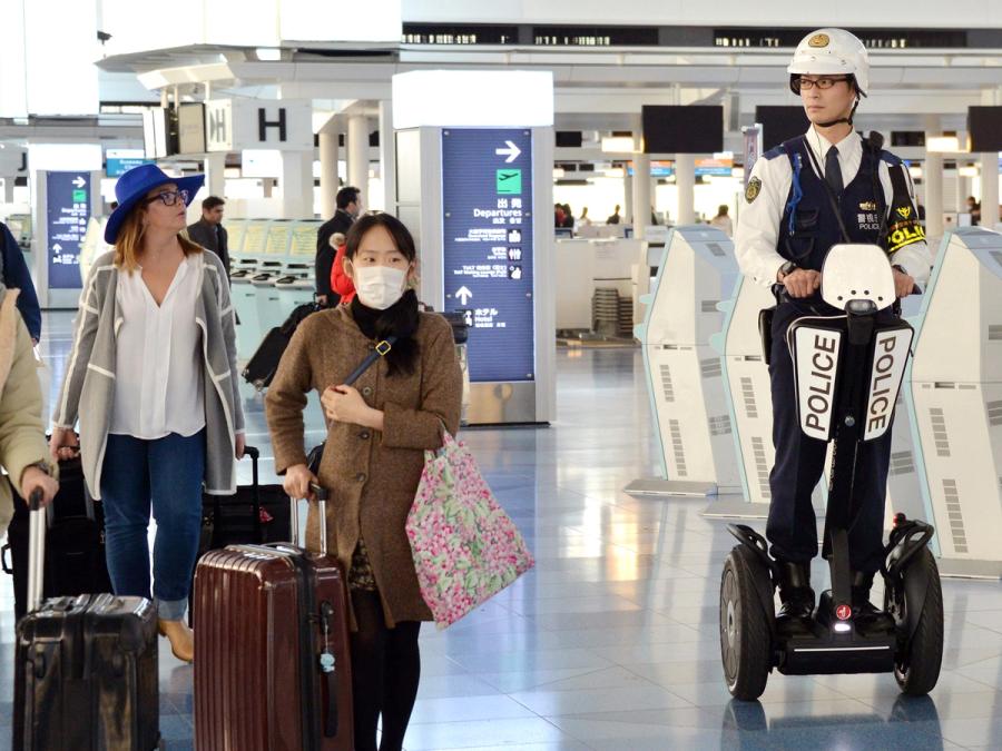 A policeman on a Segway rides past travellers in an airport.