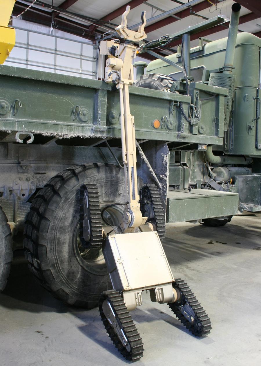 The robot climbs a military truck. It has a large extension coming out of the top to see into the truck with.