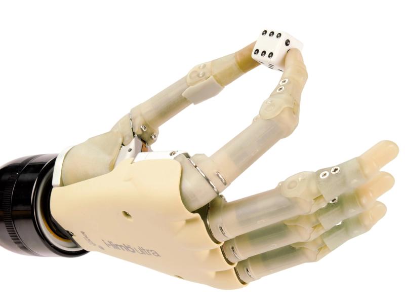 Close-up of a flesh colored robotic hand system pinching a die between two fingers.