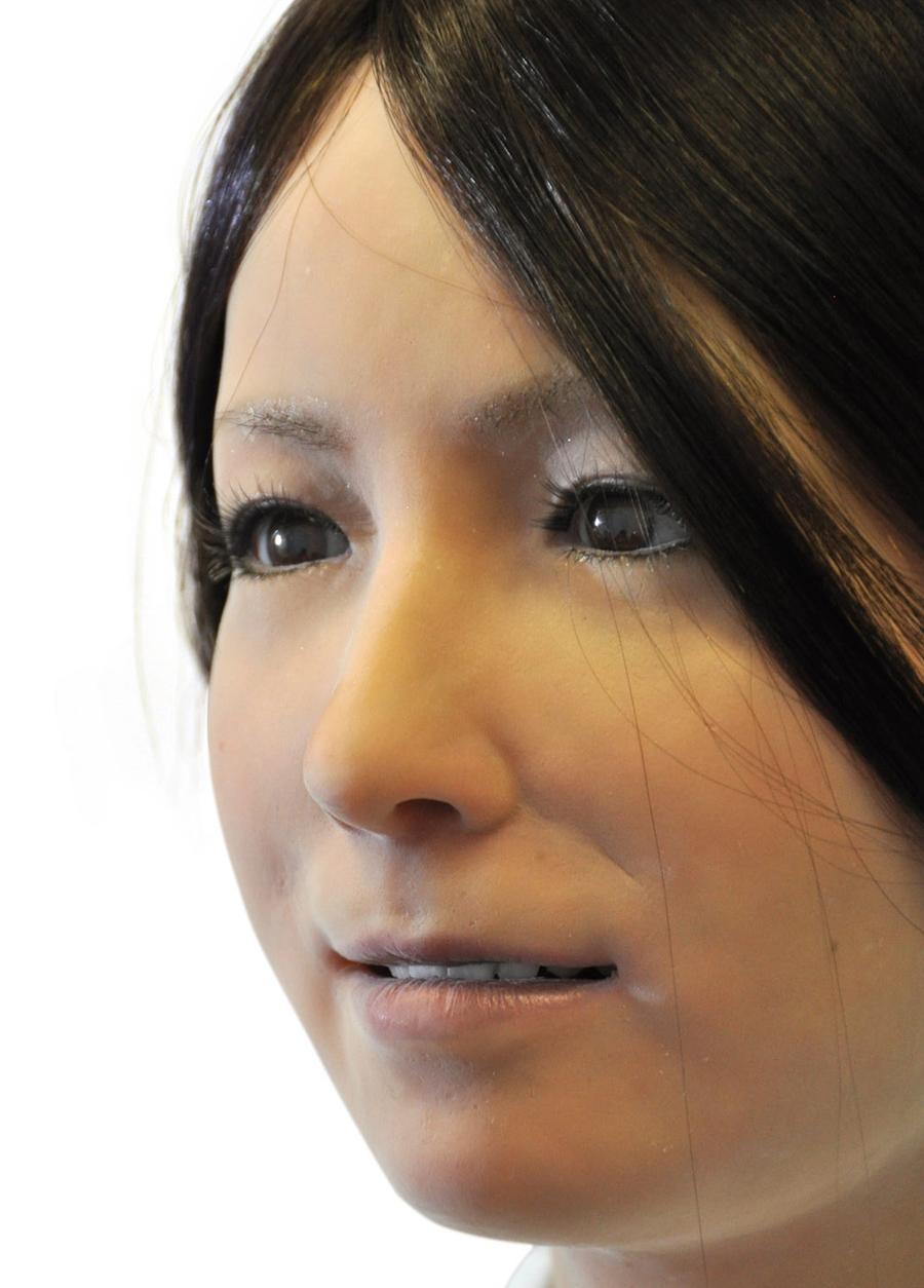 Close-up of the robots face with brown eyes, brown hair, pink lips and golden skin.