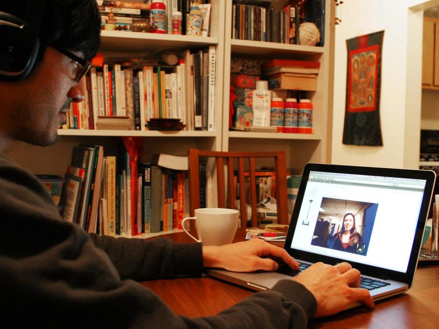 A man in glasses looks at a laptop, which displays a woman, as seen through the eyes of the robot.