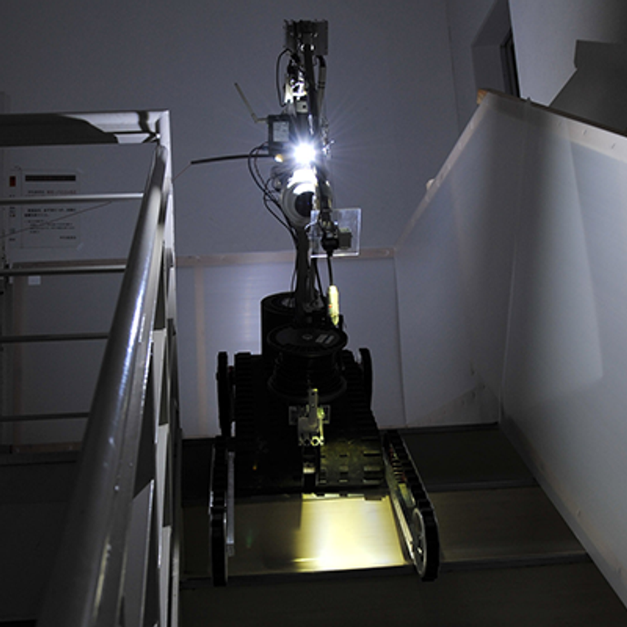 A robot on tracked wheels shines a light from it's top arm as it descends down stairs.