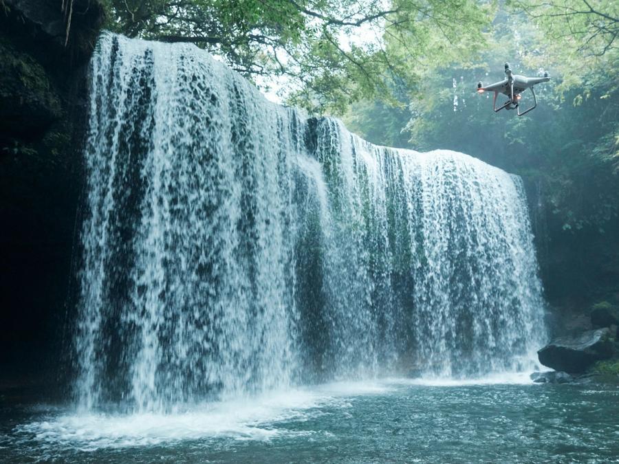 A drone flies next to a large waterfall and water.