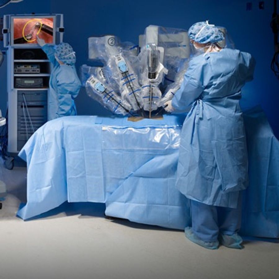 Two people in doctors scrubs and masks move a surgical robot with multiple arms with devices over a patient.