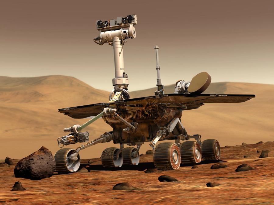 Spirit, a large rover with six tracked wheels, solar panels, and a neck with cameras like a face, is seen on Mars.