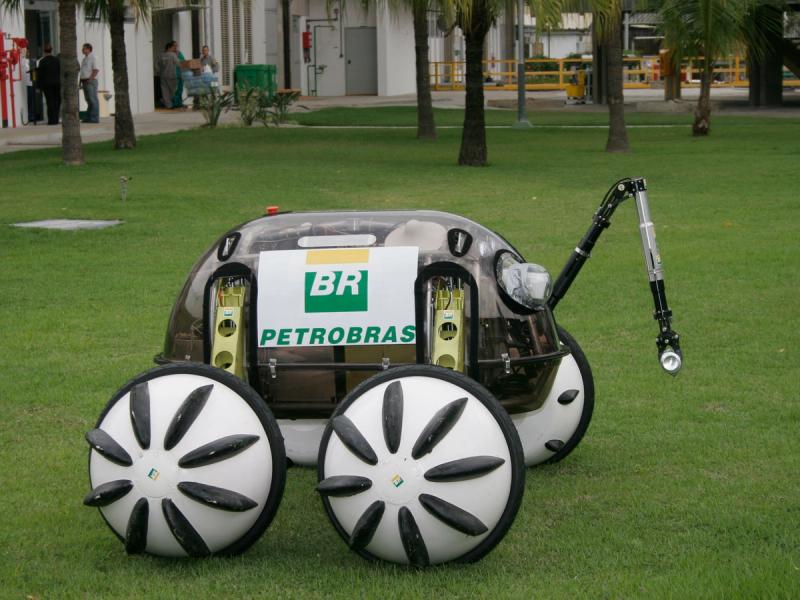 A robotic vehicle consisting of a base with electronics and an articulated arm with four large black and white wheels.