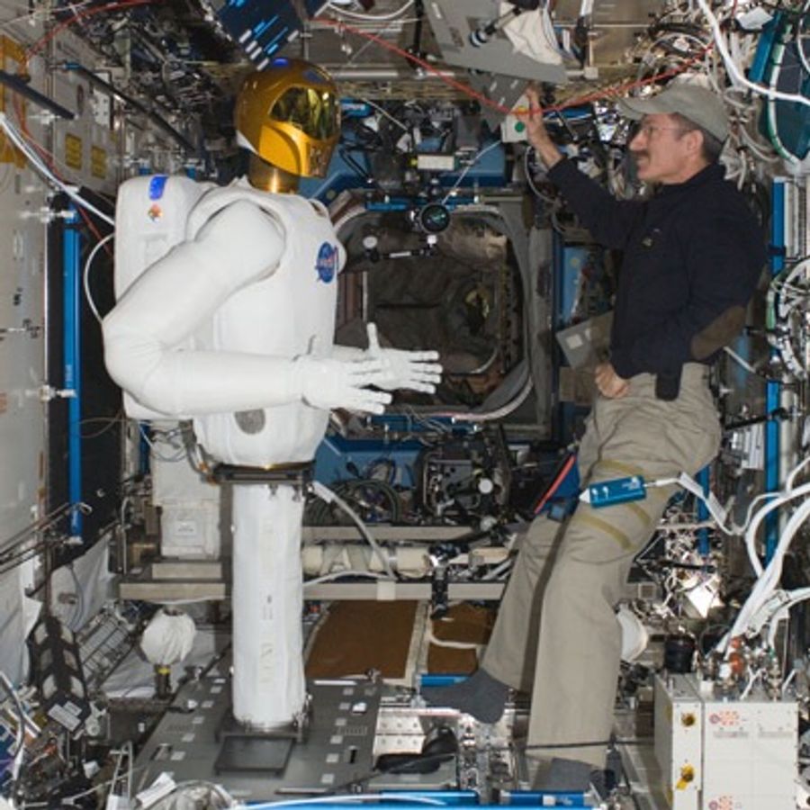 Astronaut stands in front of humanoid robot at the International Space Station.