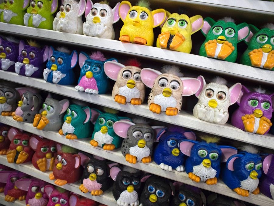 Almost 40 colorful Furby robots are seen on 5 shelves.