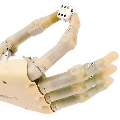 Close-up of a flesh colored robotic hand system pinching a die between two fingers.