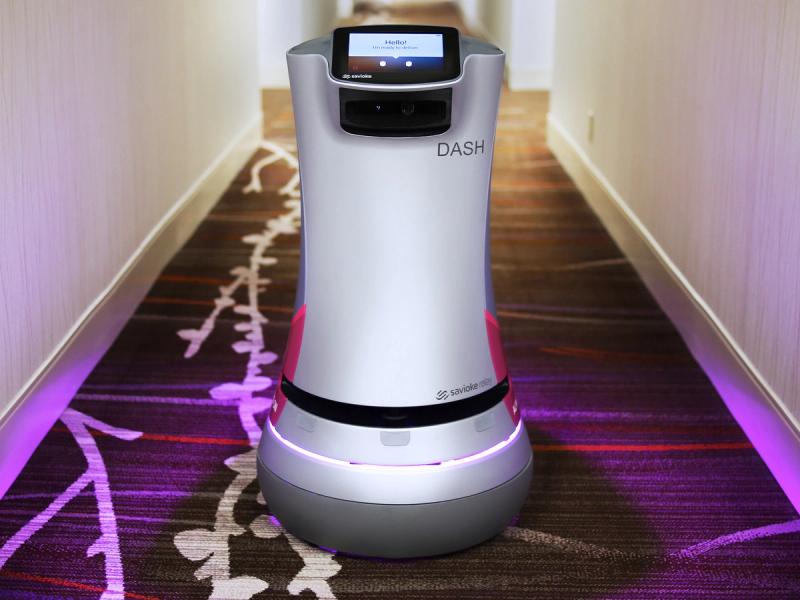 一个圆柱形机器人，位于一个带有粉红色光环的轮式平台上。它的顶部有一个触摸屏，可以作为机器人的脸。它的名字叫DASH。