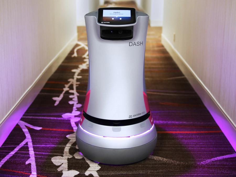 A cylindrical robot on a wheeled platform which has a ring of pink light. It's top has a touch screen that doubles as the robots face. It's name is DASH.