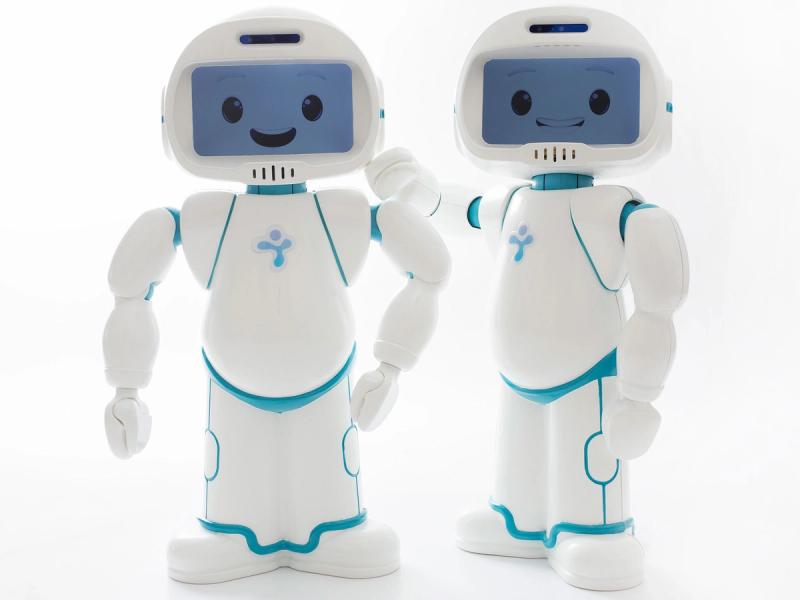 Two friendly little humanoids pose together. They have simple white bodies, arms, and a rounded faceplate holding a screen displaying a smiling cartoonish face.