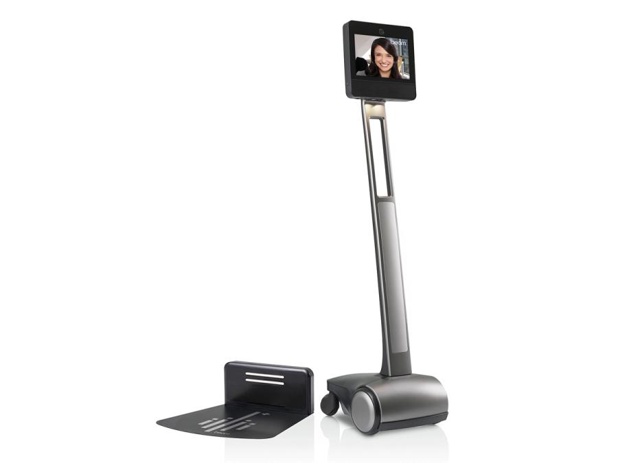 A wheeled telepresence robot with a display on top that shows a smiling woman stands next to a base.