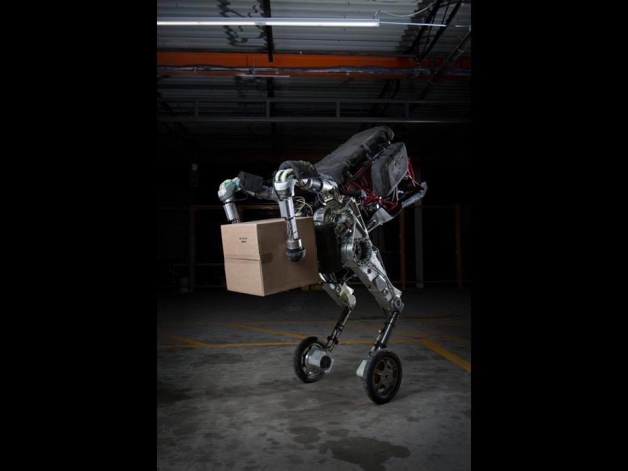A two wheeled robot balances while holding a package between two balled robotic arms.