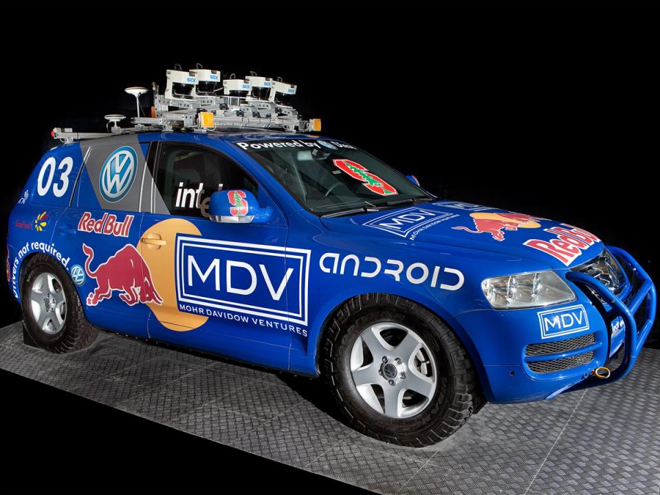 A blue, logo covered self-driving car with a roof rack full of electronics.