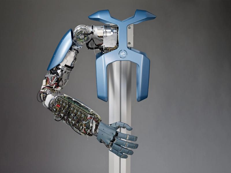 The robotic arm and hand is displayed attached to a metal base. 