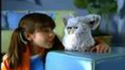 A girl with brown hair looks at a white Furby.