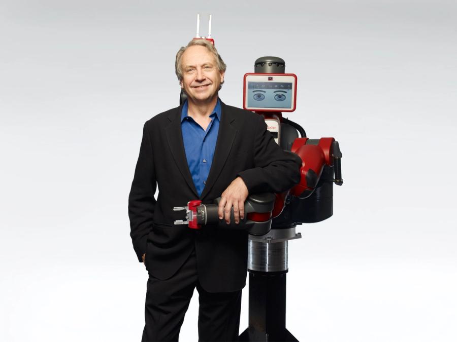 Baxer, a human sized red robot holds up two "bunny fingers" behind Rodney Brooks, a smiling man standing next to it.