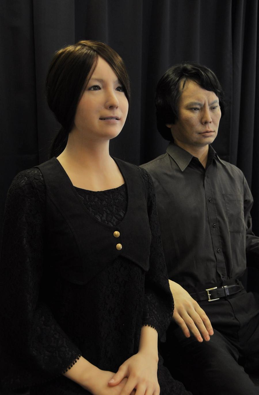 A very realistic looking female and male android sit together.