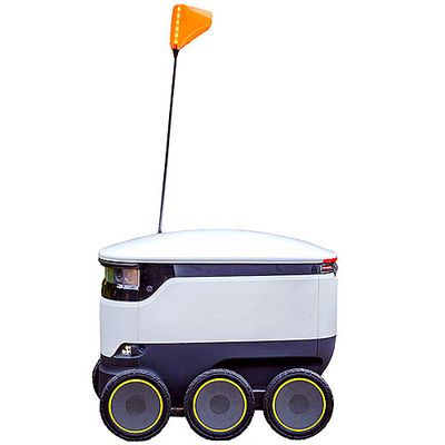A white boxy mobile robot on six wheels with a narrow antenna with an orange flag on top.