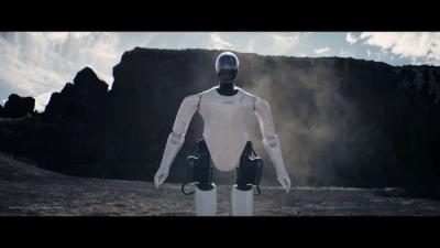 A humanoid robot with a sleek white and black body stands in a desert landscape with a wall of rock in the background.