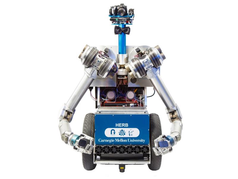 A two-wheeled robot with a blue base labelled HERB features a torso, two articulated arms with gripping fingers, a blue pipe-like neck with a black bowtie on it, and a platform for a head that includes a camera system.