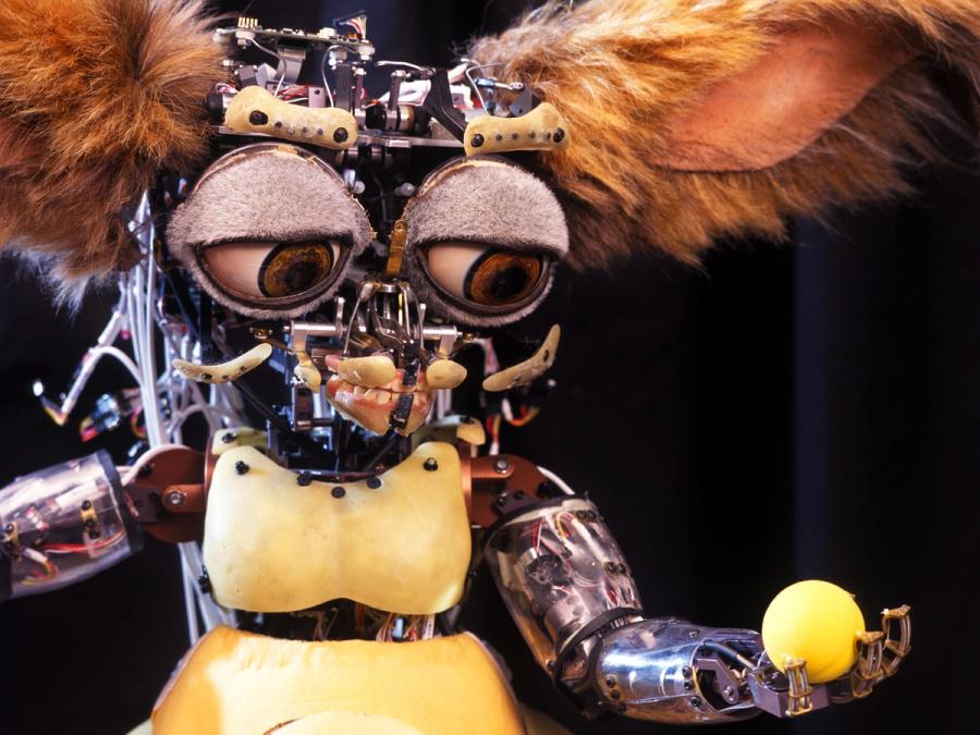A view of the robot without its fur shows exposed electronics. Leonardo holds a yellow ball in its hand.