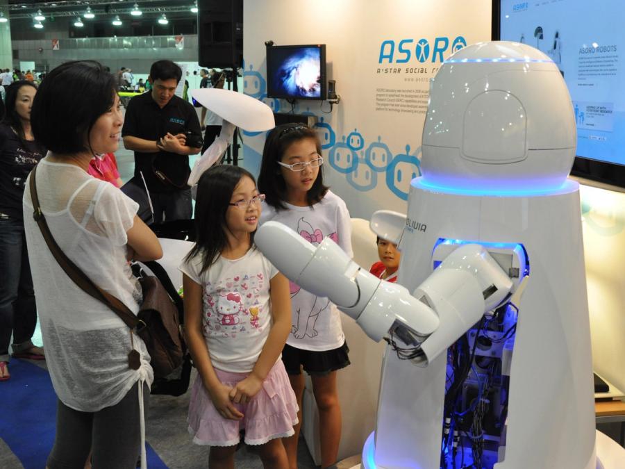 Two children and their mom interact with the robot at a trade fair.