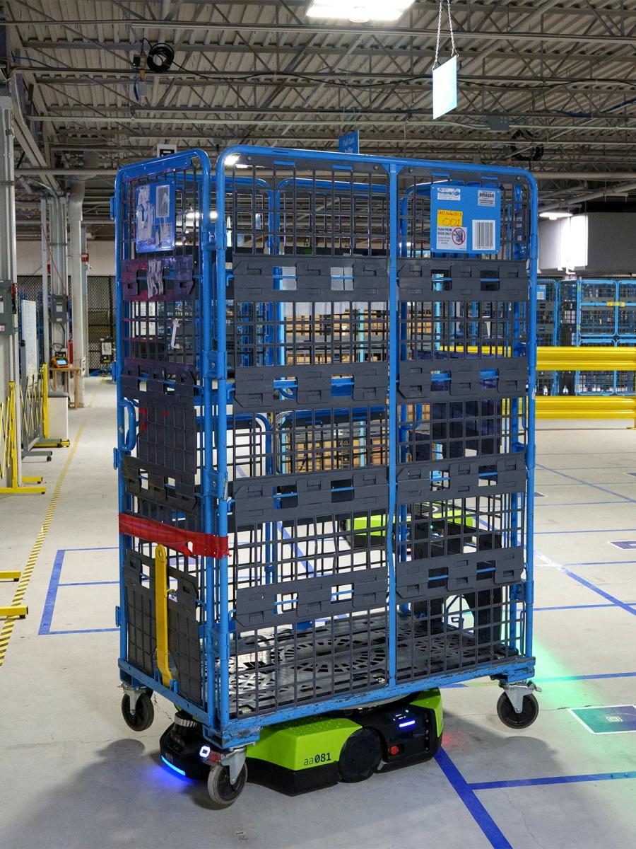 A green mobile robot carries a tall blue wheeled shelf.