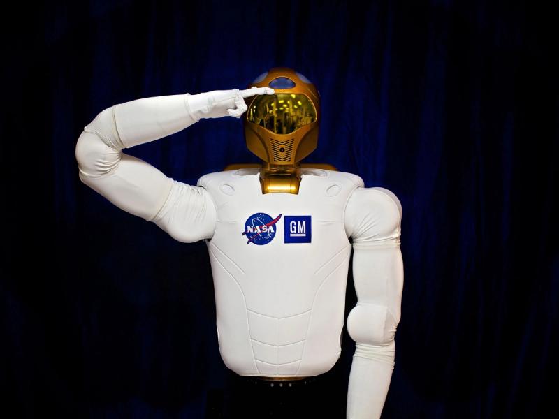 A robot astronaut torso with a gold helmet head, and a soft, white body. It holds one hand up to its head in salute.