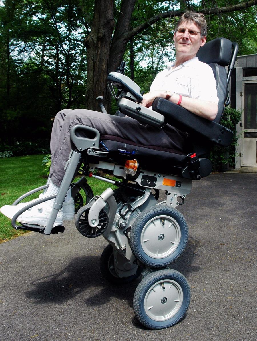 A man sits in a robotic wheelchair that is elevated on double height wheels.