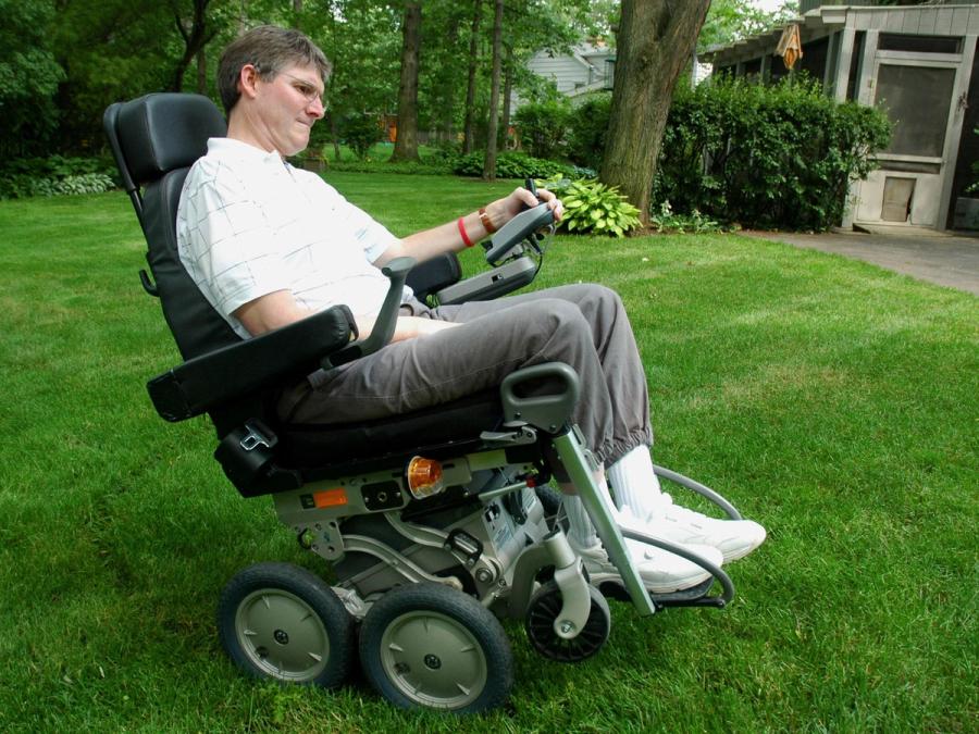 A man guides his robotic wheelchair across a green lawn.