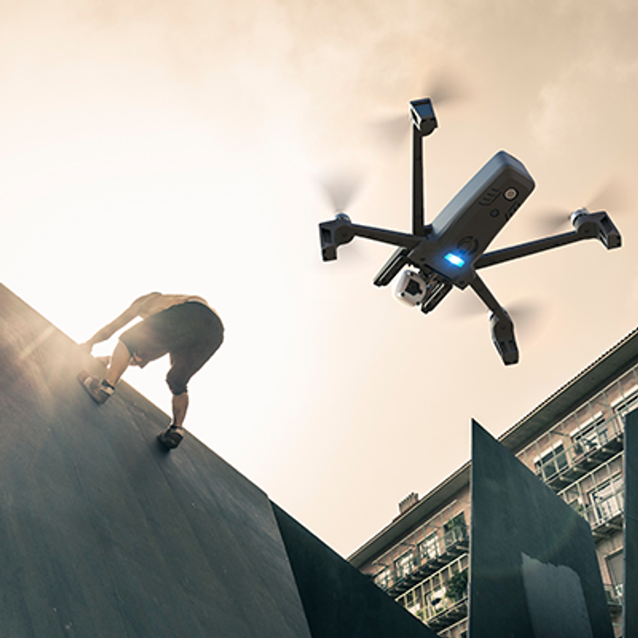 A drone hovers below a person climbing a wall.