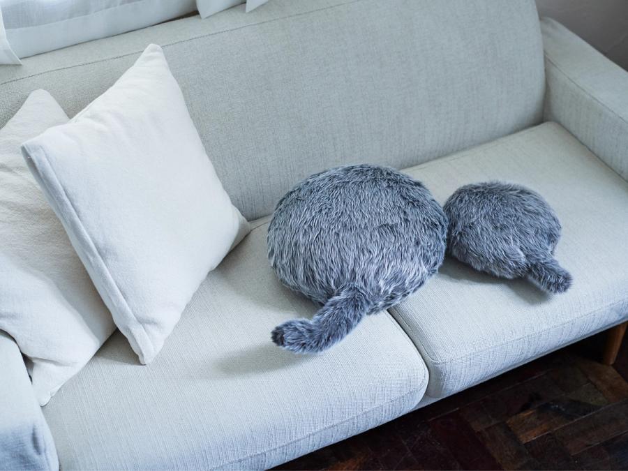 Two round cushions with tails, covered in soft looking gray fur, sit on a white couch.