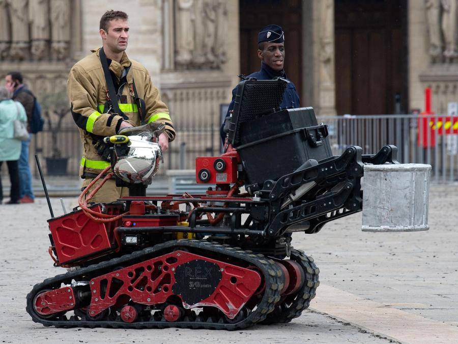 A firefighter and the robot stand outside a building.
