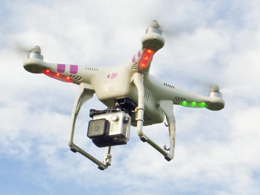A beige drone with a large camera and glowing lights in flight.