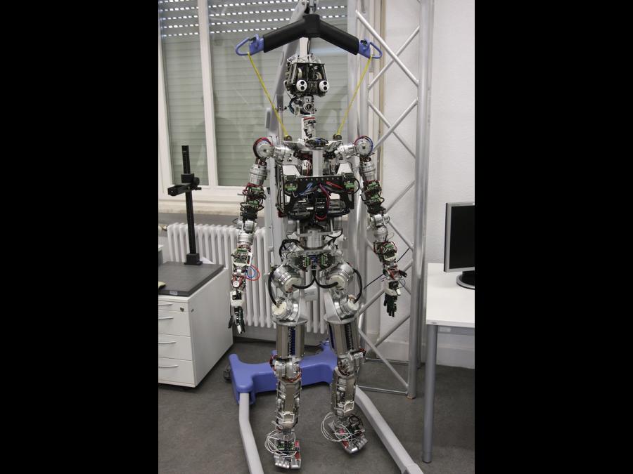 The frame of a humanoid robot stands with an overhead harness holding it up.
