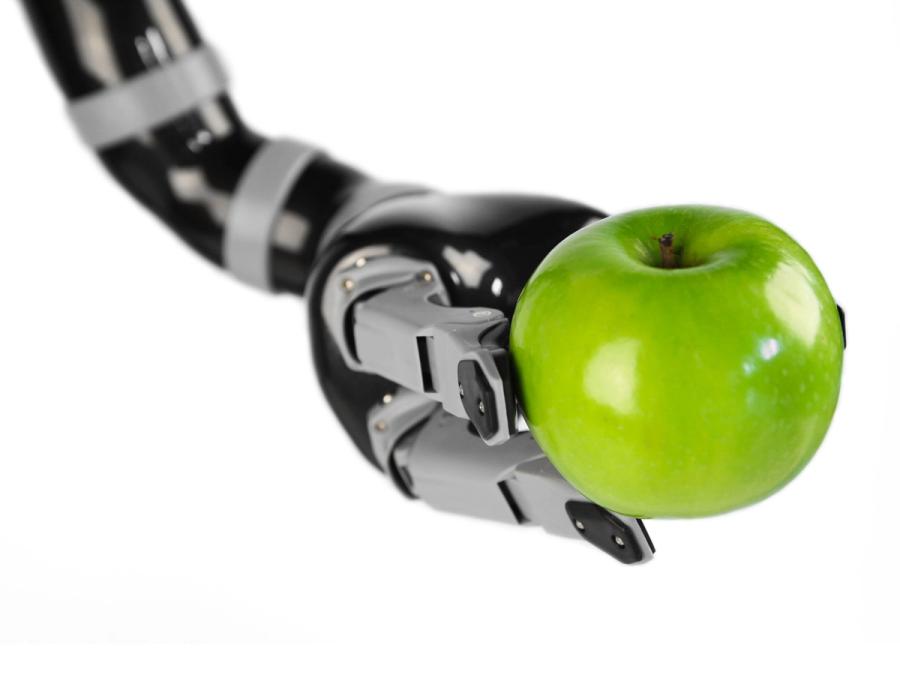 A three-fingered robotic arm squeezes an apple.