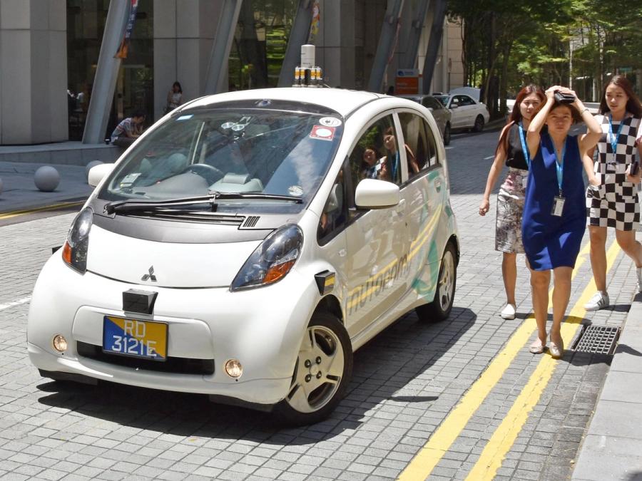 A self driving car on the street with three women standing next to it.